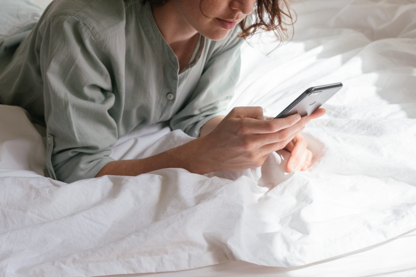Woman checking phone while in bed. Avoid online platforms in the morning to have a healthy relationship with social media. 